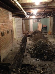 An unfinished basement with a gaping hole cut in the floor. 