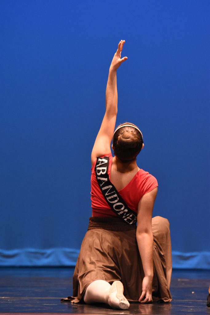 A dancer kneels. The word "abandonment" is across her back. 