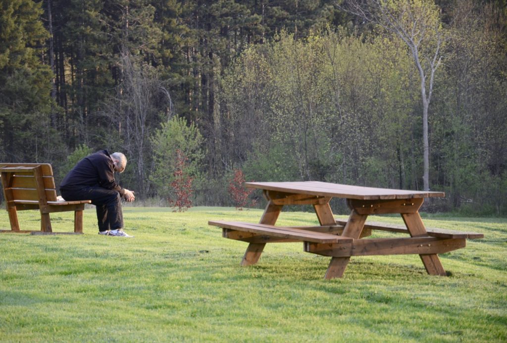 A man sits on a bench in a field. 