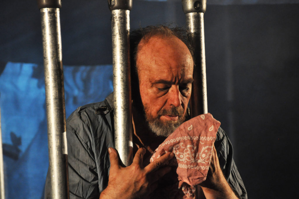 A man holds a cloth through the bars of a prison cell. 