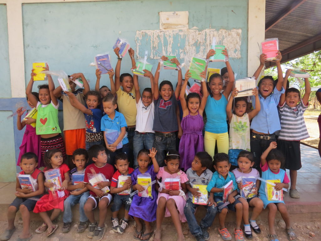 Kids hold up notebooks and school supplies. 