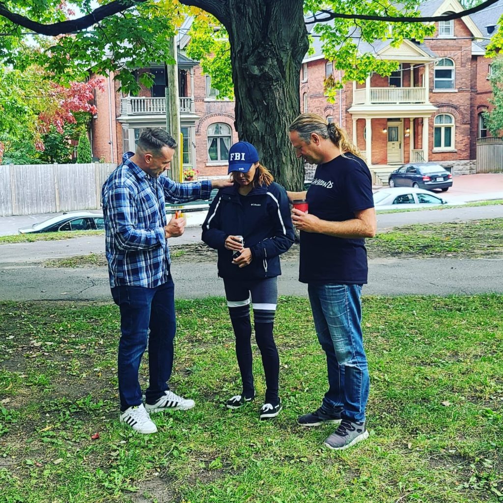 Two men pray for a woman in a park. 