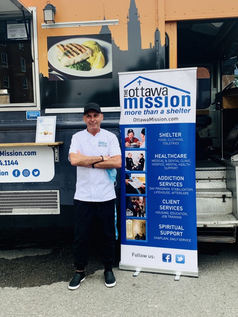 A chef stands in front of a charity food truck. 